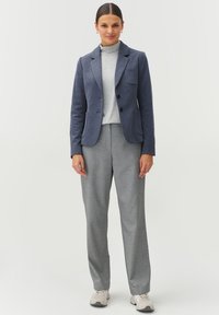 Tumes blazers klappidega ja kahe nupuga, kaasas heledat halli kõrge kaelusega särk ja kohandatud hallid püksid. Jalatsiteks on beežid tossud.