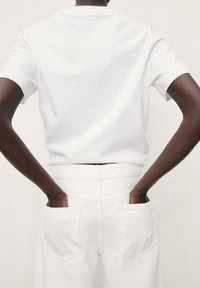 White short-sleeve t-shirt with a clean silhouette, paired with white pants featuring back pockets. Smooth texture, casual design.