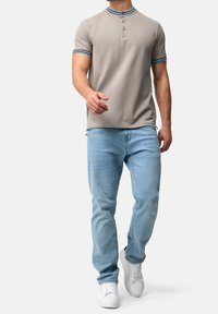 Jasnoszary polo z krótkim rękawem z trzema guzikami i niebieską lamówką kołnierzyka. W połączeniu z jasnoniebieskimi dżinsami i białymi trampkami.
