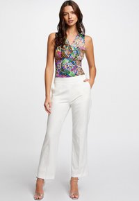 Bodysuit sin mangas con estampado floral en colores vibrantes, combinado con pantalones blancos de corte ajustado. Presenta un diseño de escote en V y una textura de tela suave.