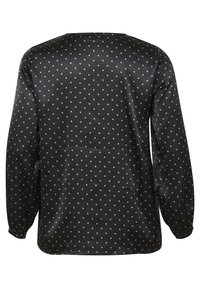 Chemise noire à manches longues avec une texture lisse, présentant un motif à pois beige clair. Comprend un col rond et des poignets élastiques.