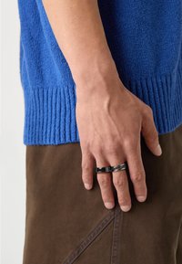 Kootud sinine kardigan ribakrae äärisega, kantud pruunide pükstega. Käes on mustad sõrmused, mis demonstreerivad materjalide ja värvide kontrasti.