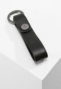 Black leather keychain with a flat strap, featuring a silver button detail and a circular metal ring for keys. Textured surface.