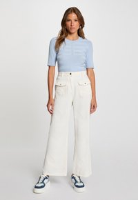 Haut à manches courtes à rayures bleu clair associé à un pantalon large crème taille haute avec poches avant et baskets à semelle blanche marine.