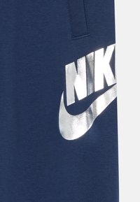 Ναυτικά μπλε Nike φόρμες με ανακλαστικό ασημί λογότυπο που διαθέτει έντονη γραμματοσειρά και σχέδιο swoosh, κατασκευασμένες από μαλακό ύφασμα.
