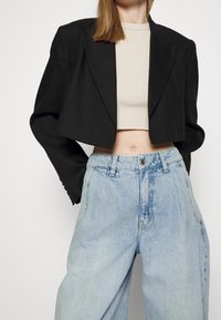 Mustat lyhyet bleiserit, joiden rakenne on selkeä, yhdistettynä korkeavyötäröisiin vaaleisiin farkkuihin, joissa on rento istuvuus ja näkyvät ompeleet.