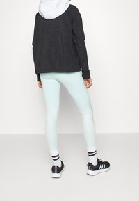 Sudadera de tiro negro salpicada, leggings verde menta claros y zapatillas deportivas negras con rayas blancas y una suela de contraste sutil.