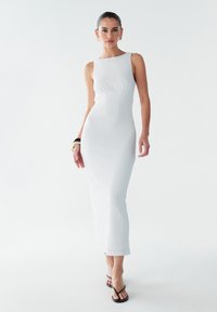 Robe midi blanche à côtes avec une silhouette ajustée, un col rond et un design sans manches. Présente une texture lisse et tombe juste en dessous de la cheville.