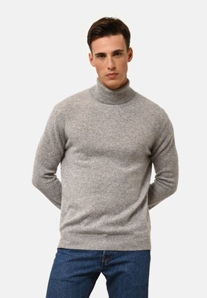 Maglione grigio a collo alto realizzato in tessuto morbido, caratterizzato da un design aderente e maniche lunghe. Indossato con jeans in denim blu.