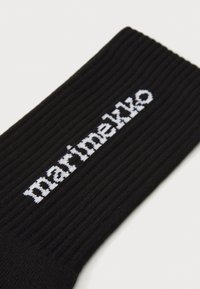 Čierna rebrovaná ponožka s bielym textovým logom "marimekko". Vyrobená z mäkkého materiálu, s pohodlným strihom a textúrovaným povrchom.