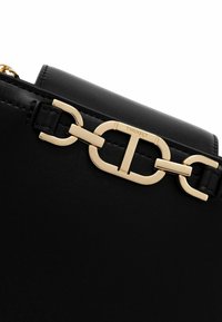 Zwarte leren tas met een goudkleurige kettingriem en een grote gouden gesp als accent. Gladde textuur met een minimalistisch ontwerp.