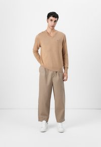 Beige v-hals trui gemaakt van zachte stof, gecombineerd met losse tan broek en witte sneakers. Eenvoudig ontwerp, minimale branding op de trui.
