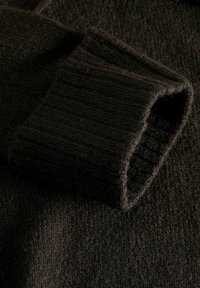 Ciemnobrązowy sweter z dzianiny z prążkowanymi mankietami, z teksturowaną powierzchnią i złożonym detalem rękawa. Miękki materiał widoczny z bliska.