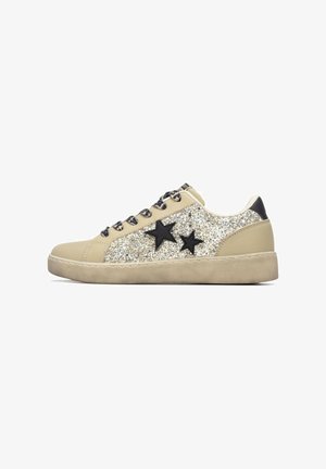 Zapatilla beige con parte superior brillante en tonos dorados y plateados, con acentos de estrellas negras y cordones redondos. Suela gruesa de goma para mayor soporte.
