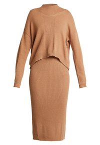 Completo a maglia in morbido color sabbia. Caratterizzato da un maglione corto a maniche lunghe con colletto alto e una gonna a costine di lunghezza al ginocchio.