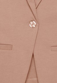 Veste beige clair en tissu lisse, dotée d'une fermeture à un bouton, de deux poches avant et d'un revers cranté.