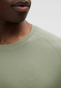 Light green textured short-sleeve shirt with a round neckline and flat seams, featuring a subtle pattern and a fitted design.