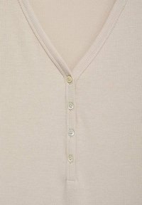 Ljusbeige ribbad stickad topp med V-ringning, som har fem knappstängningar och en texturerad yta. Mjuk tyg med subtila mönster.