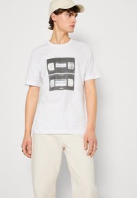 Weißes Baumwoll-T-Shirt mit einem Grafikdesign, das zwei VHS-Kassetten zeigt. Text mit den Aufschriften "Meine schlechten Tage" und "Meine guten Tage" in Blau. Lässige Passform.