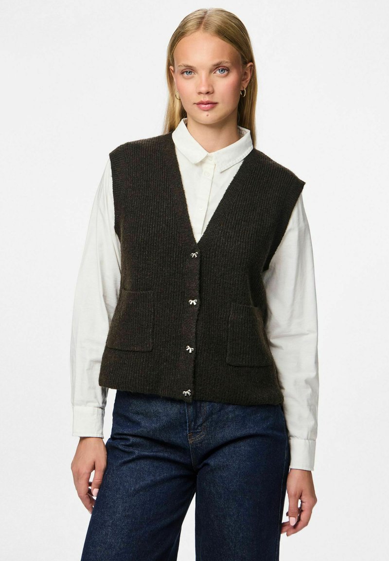 Tmavě hnědý pletený svetr s výstřihem do V, se předními kapsami, pěti knoflíky a texturovaným povrchem. Nosený přes bílou košilovou košili.