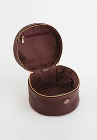 Round cosmetic bag in textured burgundy material, featuring a gold zipper and interior pocket. Lined with smooth, dark fabric.