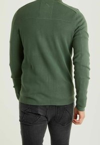 Grön långärmad tröja med ribbad textur och kontrasterande sömnad, sedd bakifrån. Matchad med svarta jeans med bakfickor.