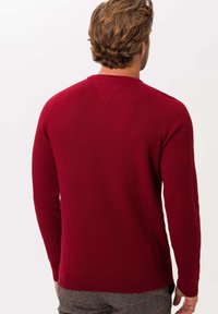 Czerwony sweter z dzianiny, z długimi rękawami, dopasowany fason i dekoltem w kształcie litery V. Ribbowana tekstura i detal przy hemie z gładkim tyłem.