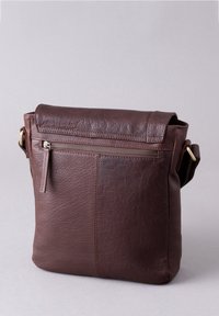Brown leather crossbody bag with a zippered front pocket, rectangular shape, smooth texture, and a single adjustable strap.
