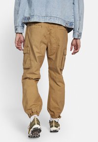 Khaki cargo pants with elastic cuffs, featuring side pockets, a round stitched detail on the back, and a textured fabric.