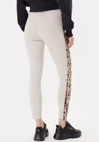 Leggings aderenti beige con strisce laterali in stampa leopardata. Tessuto liscio, lunghezza alla caviglia, abbinate a sneakers nere.