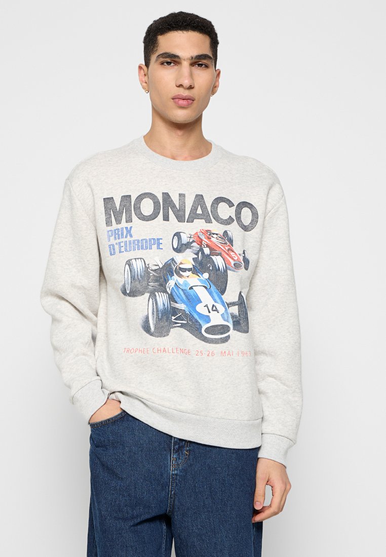 Grauer Sweatshirt mit einem vintage Rennsportgrafik, die blaue und rote Autos zeigt, Rundhalsausschnitt und gerippte Bündchen und Saum. Der Text enthält "MONACO" und Veranstaltungsdetails.