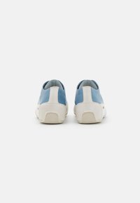 Zapatillas azul y blancas con un upper liso, talón en contraste, suela texturizada y sin marcas visibles en la vista trasera.