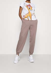 Vit t-shirt med en färgglad hjortgrafik, kombinerad med ljusbruna sweatpants med ankle cuffs och elastisk midja. Vita sneakers.