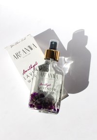 Flacon pulvérisateur en verre transparent avec bouchon doré, rempli d'eau de lavande et de cristaux d'améthyste. Boîte blanche avec texte noir en arrière-plan.