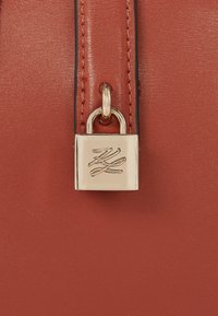Red leather handbag with a smooth texture. Features a gold padlock accent with a logo. Includes a contrasting black zipper detailing.