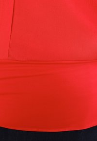 Top rosso in tessuto elasticizzato con una consistenza liscia, caratterizzato da un design aderente e una fascia larga sul fondo.