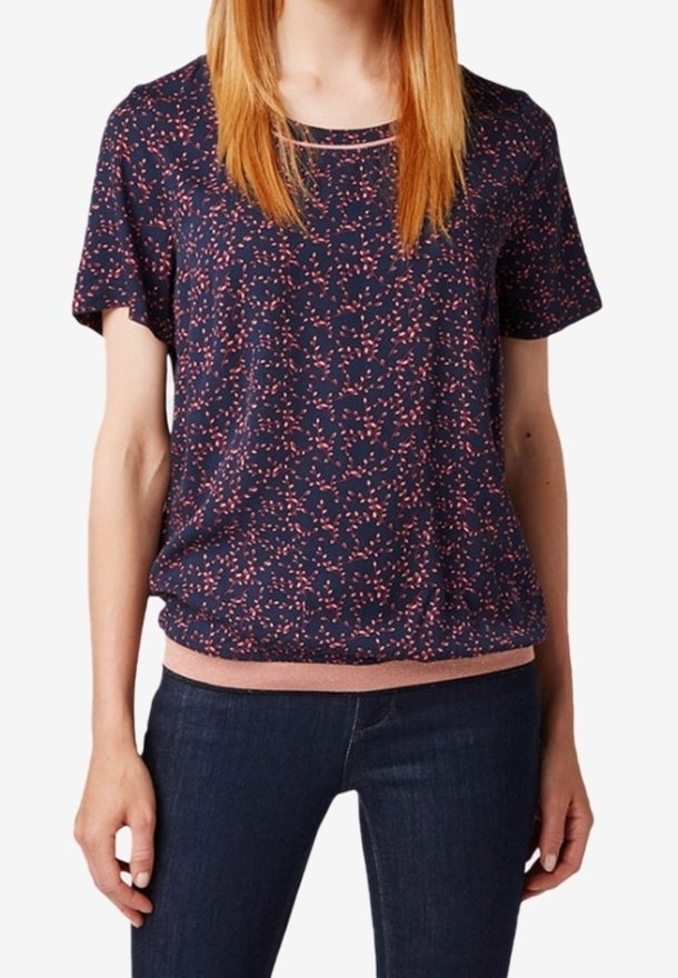 Femme portant un haut bleu marine à manches courtes avec un motif tacheté rose et un ourlet rose, associé à un jean bleu foncé.