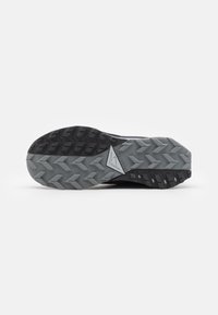 Suola di scarpa da trail running nera con un motivo in gomma grigia testurizzata, caratterizzata da un logo triangolare e scanalature profonde per aderenza e trazione.