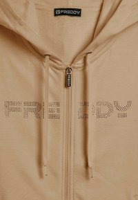 Felpa beige con zip e coulisse, con la scritta in strass "FREDDY" sul petto e tirazip e etichetta con il marchio "FREDDY".