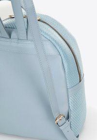 Světle modrá kabelka s hladkými a tkanými texturami, zlatým zipem a nastavitelným popruhem na bílém pozadí.