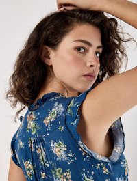 Blå blommig blus med korta volangärmar, med en texturerad tyg och en samlad bakdesign med blommönster i olika färger.