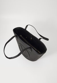 Black leather tote bag with two long handles, textured surface, interior zip pocket, and additional compartments for organization.