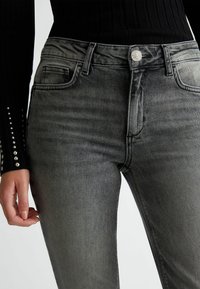 Vaqueros de mezclilla gris con un diseño ajustado, que cuentan con un estilo de cinco bolsillos, una bragueta de botón y un ligero desvanecimiento en la parte frontal.