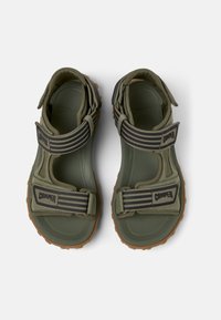 Sandales vert olive avec des brides ajustables, semelles en caoutchouc et semelles intérieures texturées. Présente un logo et des détails rayés contrastants.