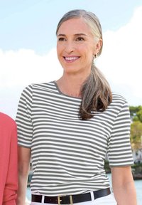 Grau-weißer gestreifter T-Shirt mit Rundhalsausschnitt und kurzen Ärmeln, kombiniert mit einem schwarzen Gürtel, getragen von einer lächelnden Frau im Freien.