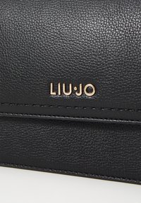 Portafoglio in pelle sintetica nera con superficie texturizzata, caratterizzato da un logo dorato "LIU•JO" e dettagli cuciti lungo i bordi.