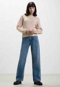 Maglione a maglia in tonalità pastello con orlo a coste, abbinato a jeans a gamba ampia e blu sbiaditi e stivali neri con plateau. Silhouette semplice e rilassata.
