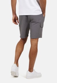 Szare kratkowane spodenki cargo z bocznymi kieszeniami i elastycznym pasem, w połączeniu z białymi sneakersami. Oferują luźny krój i teksturowany materiał.