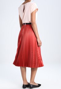 Falda plisada en rojo, hecha de una tela suave, con una cintura ajustada y un cinturón negro. Top rosa de manga corta con un detalle de apertura en la espalda.