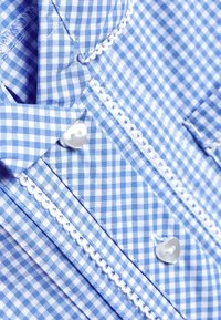 Blau-weißes Gingham-Stoff mit strukturiertem Erscheinungsbild, verziert mit weißen Spitzenbesätzen und herzförmigen Knöpfen.